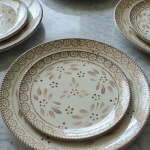 May include: A collection of cream-colored ceramic plates with a brown floral design. The plates have a decorative border and are arranged in a nested pattern. The plates are of varying sizes.