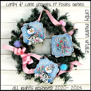 May include: Three hand-painted wooden ornaments featuring snowmen and candy canes on a blue background with white snowflakes. The ornaments are hanging on a green wreath with pink ribbon and white wooden background. The text "candy cane snowies n' posies ornies" is at the top of the image and "cindy mann vitale" is on the right side of the image. The text "all rights reserved 2020-2025" is at the bottom of the image.