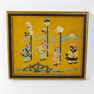May include: A framed needlepoint artwork depicting a scene with five figures in traditional Chinese clothing. The figures are standing on a bridge over a body of water, with a yellow sky and clouds in the background. The artwork is framed in a gold frame with a black inner border.