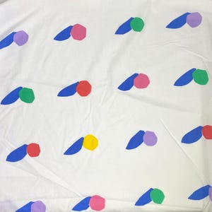 Peut inclure: Un tissu blanc présentant un motif répétitif de petites formes bleues pleines en forme de feuilles, associées à des cercles géométriques multicolores dans des tons rose, vert, rouge, jaune et violet, disposés en grille sur la surface.