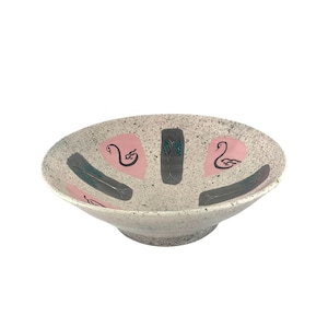 May include: A large, white ceramic bowl with a speckled glaze. The bowl has a wide, shallow base and features a pink and gray design with stylized birds and trees.