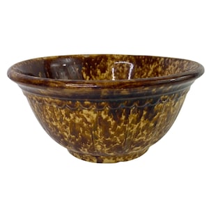 Pode incluir: Uma tigela de mistura de cerâmica envidraçada em marrom e amarelo com uma borda festonada. A tigela tem um esmalte marrom e amarelo.