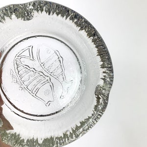 Puede incluir: Cenicero de vidrio transparente con borde texturizado y un diseño en relieve de dos peces en el centro.