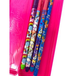 May include: A bright pink pencil case holds several colorful pens. The pens feature various designs, including rainbows, unicorns, and deer. The pens are in shades of blue, purple, pink, and green.
