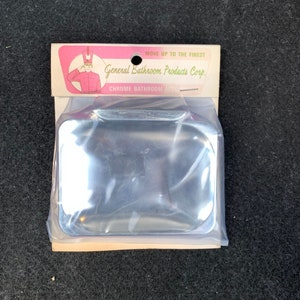 May include: A chrome bathroom accessory, square-shaped, packaged in clear plastic. The packaging includes a cardboard header with the text "General Bathroom Products Corp." and an illustration of a person in a red uniform saluting.