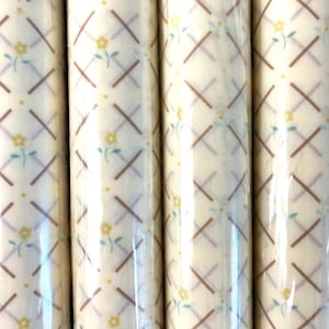 Op de afbeelding: Vier rollen wit cadeaupapier met een bruin en paars kruispatroon en kleine gele bloemen.