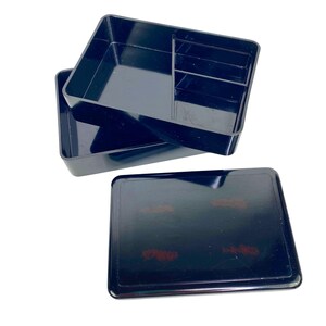 Op de afbeelding: Zwarte plastic organizer met een rechthoekige vorm. De organizer heeft meerdere compartimenten en een deksel. De bovenste lade heeft verschillende verdelers. Het deksel is effen zwart. De organizer is ontworpen om kleine items in op te bergen.