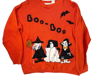 Puede incluir: Jersey naranja de Halloween con la palabra "Boo-Boo" en letras negras. El jersey presenta imágenes aplicadas de una bruja, un fantasma y un vampiro. También hay dos murciélagos negros aplicados.