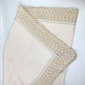 Puede incluir: Un mantel de lino blanco con un delicado borde de encaje crema.