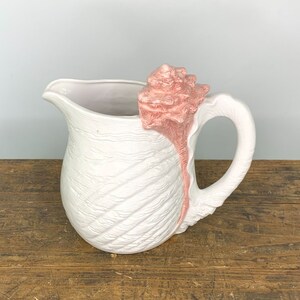 May include: White ceramic pitcher shaped like a seashell with a pink seashell on top.