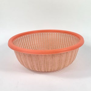 May include: A pink plastic colander with a slightly darker pink rim. The colander is made of a woven mesh pattern.
