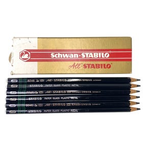 May include: A set of six black Schwan-STABILO All-STABILO pencils with a gold and red cardboard box. The pencils feature white text indicating they are for paper, glass, plastic, and metal, with model numbers 8046 and 8040 printed on the barrels.
