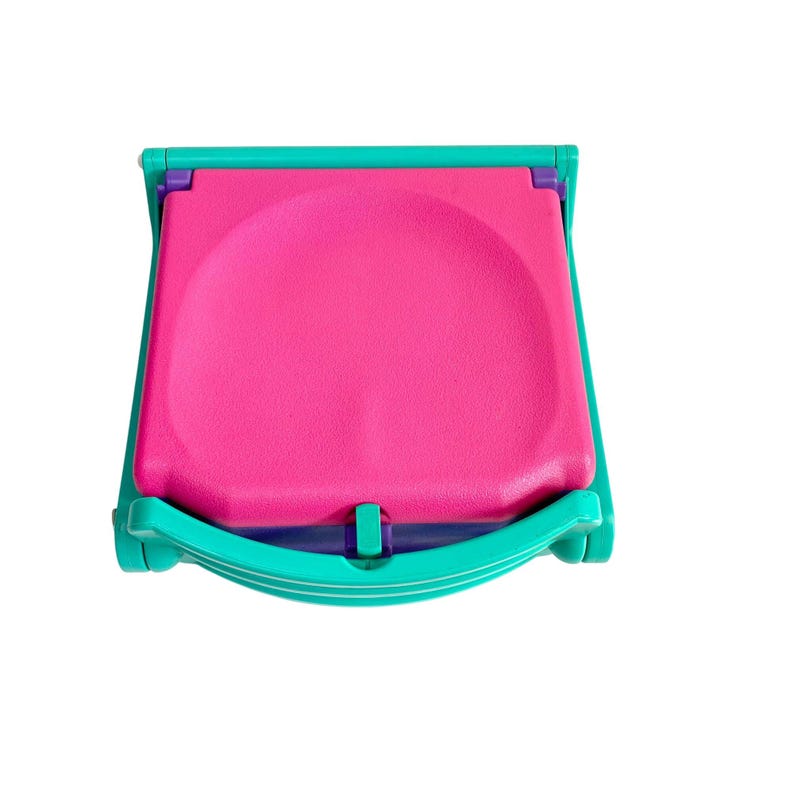 Puede incluir: Una silla plegable de color turquesa y morado con un asiento rosa. La silla est&aacute; cerrada y plegada.