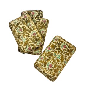 May include: Set of four rectangular trays with a floral pattern. The trays feature a cream-colored background with a repeating design of green, gold, and red flowers and leaves. The edges of the trays are a darker gold color.