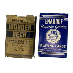 Op de afbeelding: Twee vintage kaartspellen. Eén is een bruine doos met het opschrift "Enardoe's Wonder Deck" met instructies voor goocheltrucs. De andere is een blauwe doos met "Enardoe Superior Quality Playing Cards" erop.