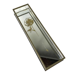 May include: Rectangular mirrored tray with a gold-colored metal frame. The mirror features a gold-colored etched rose design. The tray is long and narrow, suitable for displaying jewelry or small items. The tray is empty.