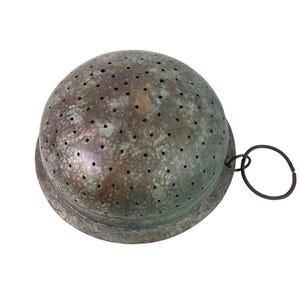 May include: A vintage, round metal strainer with numerous small holes. The strainer has a tarnished, aged appearance with a dark ring handle attached. The base is a slightly wider, circular shape. This kitchen tool is designed for straining liquids.