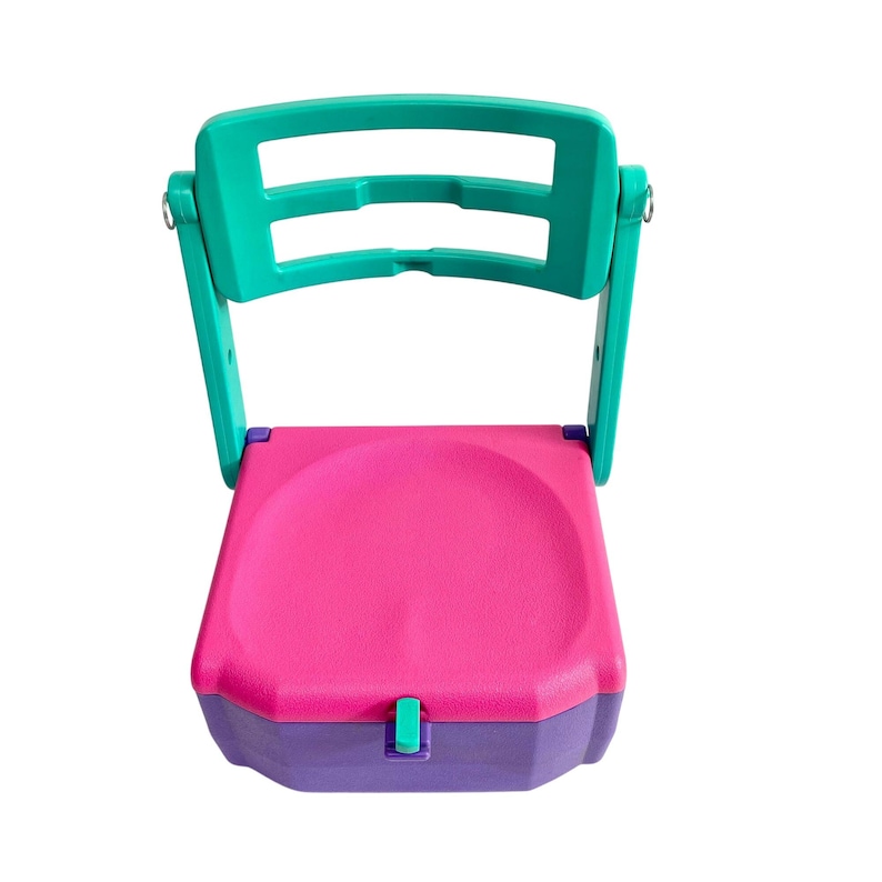 Puede incluir: Una silla plegable con un respaldo turquesa y un asiento rosa. La silla tiene una base morada y un cierre turquesa.