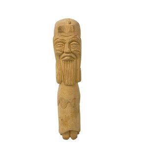 May include: A carved wooden figurine of an elderly man with a long beard and a hat. The figure is light brown in color and has detailed facial features, including carved eyes, nose, and mouth. The figure is standing upright and appears to be a decorative item.