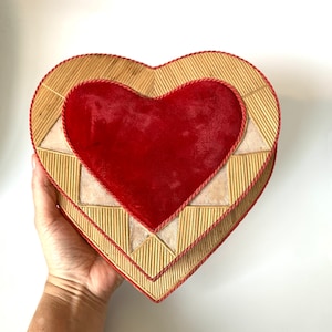 May include: A heart-shaped box with a red velvet interior and a woven straw exterior. The box is decorated with a geometric pattern and a red trim.