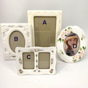 Puede incluir: Cuatro marcos de fotos de cerámica blanca. El marco A es rectangular con un patrón de corazones y puntos. El marco B es ovalado con un diseño de rosas. El marco C tiene dos aberturas y detalles florales. El marco D es ovalado con un diseño floral y una foto.