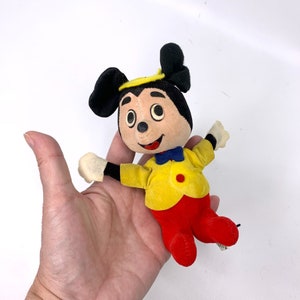 May include: A vintage plush Mickey Mouse toy wearing a yellow jacket, red pants, and a blue bow tie. The toy has black ears and a black nose.