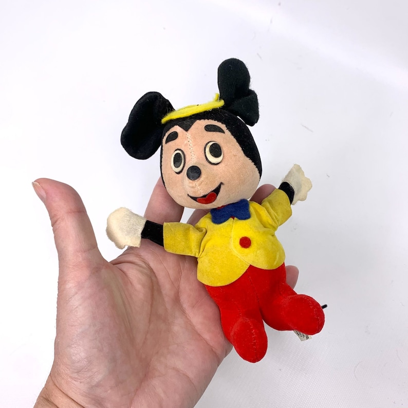 May include: A vintage plush Mickey Mouse toy wearing a yellow jacket, red pants, and a blue bow tie. The toy has black ears and a black nose.