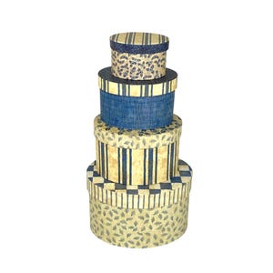 May include: A stack of four round decorative boxes in varying sizes. The boxes feature blue and cream patterns, including stripes, leaf motifs, and a checkered design. The lids and sides have coordinating patterns.