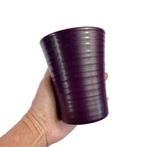 May include: A purple plastic planter with a ribbed design. The planter is being held in a person's hand.