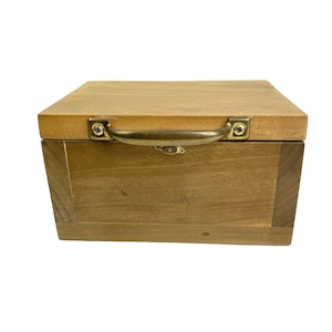 May include: A wooden box with a brass handle. The box is closed and has a light brown finish.