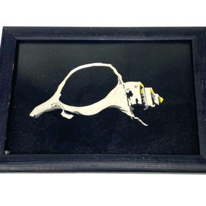 May include: A framed painting of a white seashell against a black background. The seashell is painted with white and gray brushstrokes, with yellow accents. The frame is black.