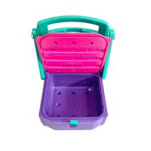 Puede incluir: Un contenedor de pl&aacute;stico morado y turquesa con una tapa rosa. La tapa tiene el texto "Drain water before transporting. Three water bottles provided." El contenedor tiene un asa en la parte superior y un cierre en la parte delantera.