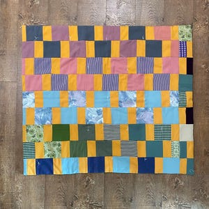 May include: A patchwork quilt with a checkered pattern. The quilt is made of various fabrics in shades of yellow, blue, green, pink, and purple.