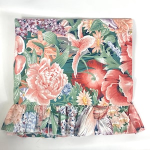 May include: A rectangular fabric piece featuring a dense floral pattern with large peach peonies, red poppies, and purple accents against a dark green background. The bottom edge is finished with a gathered, ruffled border of the same floral print.