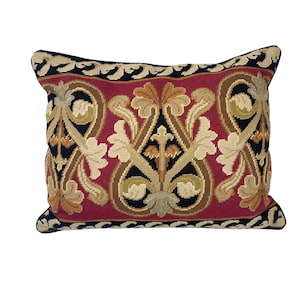 May include: Rectangular decorative pillow with a red background and an ornate floral design in beige, brown, and black. The pillow has a black border with a repeating pattern. A decorative accent for a sofa or bed.