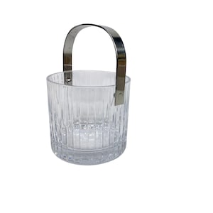 Puede incluir: Una cubitera transparente, cilíndrica, con detalles de estrías verticales. Cuenta con un asa plateada brillante que se arquea sobre la parte superior. La cubitera está diseñada para contener hielo y mantener las bebidas frías. Fondo blanco.