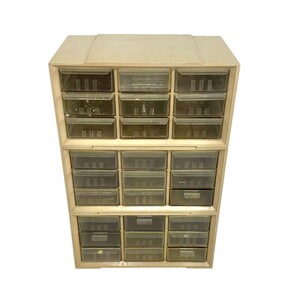 May include: A beige plastic storage cabinet featuring three stacked sections with a total of twenty-seven small, clear, rectangular drawers. Each drawer has a molded handle and a transparent front, allowing for visibility of the contents inside.