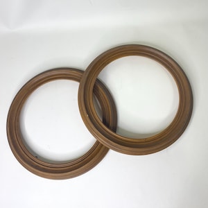 Può includere: Due cornici rotonde in legno, di colore marrone caldo. Le cornici si sovrappongono, evidenziando la loro forma e il design dettagliato del bordo. Sono poste su uno sfondo bianco. Ogni cornice ha un diametro di circa 30 cm.