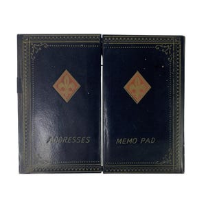 Könnte beinhalten: Zwei marineblaue Adressbücher und Notizblöcke. Jedes Buch hat ein goldenes Fleur-de-Lis-Design in Diamantenform. Die Bücher sind mit goldenem Filigran und den Wörtern "Adressen" und "Notizblock" verziert.