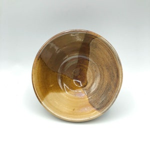 May include: A brown ceramic bowl with a glazed finish. The bowl has a unique swirl pattern in shades of brown and tan.