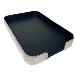 May include: A rectangular tray featuring a matte black interior base and a smooth, metallic silver exterior rim. The tray has rounded corners and a low-profile design with a continuous metal border that frames the flat, dark surface.