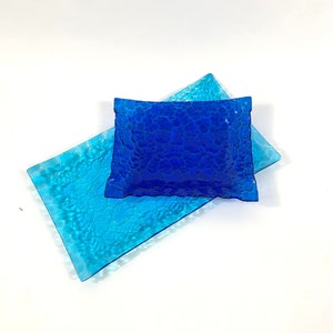 May include: Two rectangular glass serving trays, one blue and one light blue, with a textured surface. The blue tray is on top of the light blue tray.