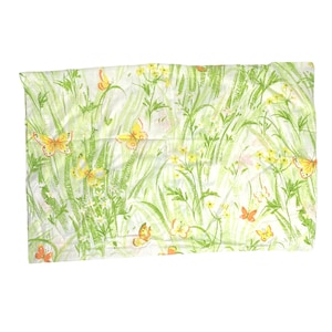 May include: A rectangular fabric piece featuring a white background with a repeating pattern of green blades of grass, small yellow wildflowers, and orange and yellow butterflies scattered across the surface in a naturalistic arrangement.