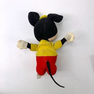 May include: A vintage plush Mickey Mouse toy with black fur, yellow shirt, and red pants. The toy has a black tail and white gloves.