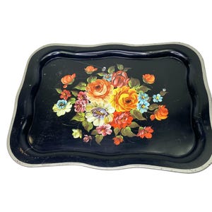 May include: A black serving tray with a scalloped edge and a floral bouquet design. The bouquet features orange, yellow, pink, and blue flowers with green leaves. The tray has a silver-colored trim.