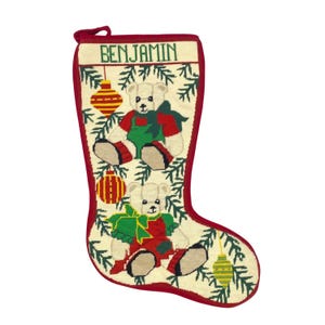 May include: A Christmas stocking with a red trim and loop. The stocking features two teddy bears wearing red and green outfits, with the name "BENJAMIN" at the top. Ornaments and pine branches decorate the stocking.