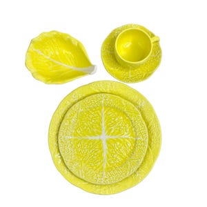 May include: A set of yellow ceramic dishes with a cabbage leaf design. The set includes a large dinner plate, a smaller salad plate, a teacup, and a saucer.