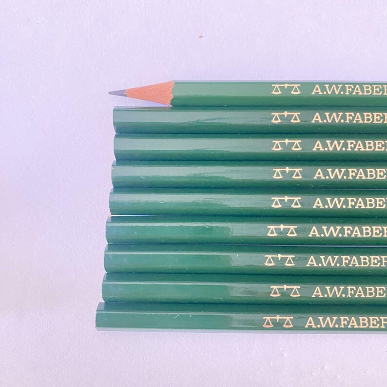May include: A stack of green pencils with the text "A.W.FABER" printed in gold. One pencil is sharpened, revealing a brown lead tip. The pencils are arranged on a white surface.