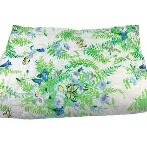 Puede incluir: Una manta acolchada blanca con un patrón floral verde, azul y amarillo con mariposas.