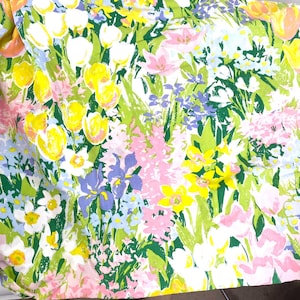 Puede incluir: Una tela floral con una vibrante variedad de flores. El diseño incluye tulipanes amarillos, flores rosas y blancas, iris moradas y follaje verde. El patrón se establece sobre un fondo blanco, creando una exhibición animada y colorida.